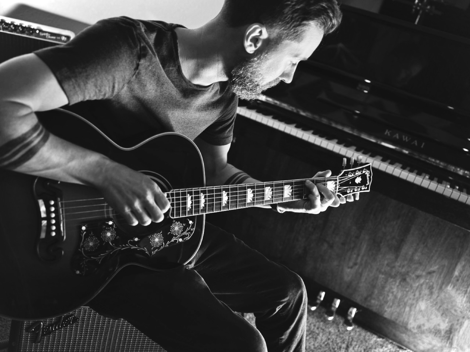 Jim English, eyes closed, playing guitar beside his piano